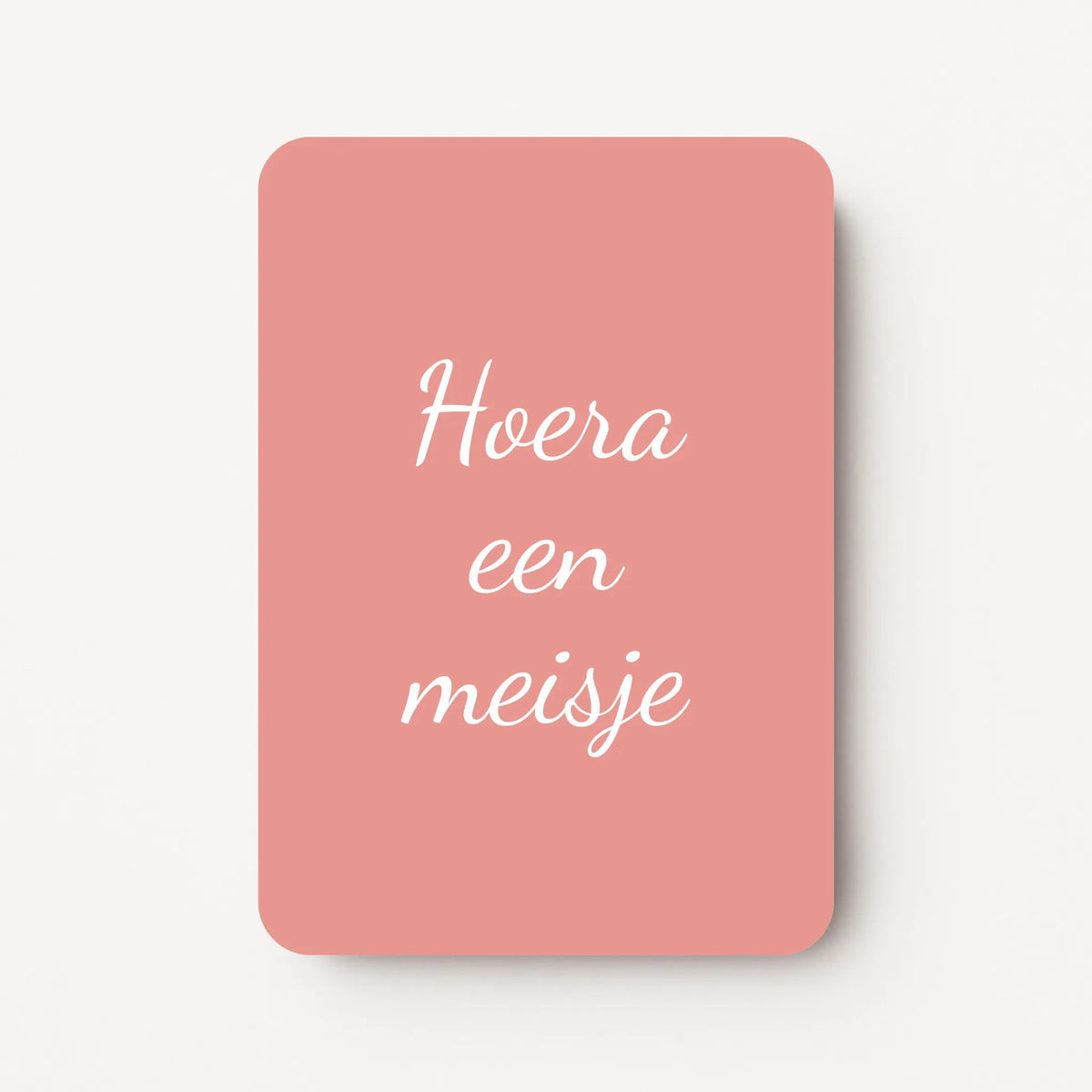 Staande minikaart met witte tekst "Hoera een meisje", minimalistisch ontwerp op een warme oudroze achtergrond.