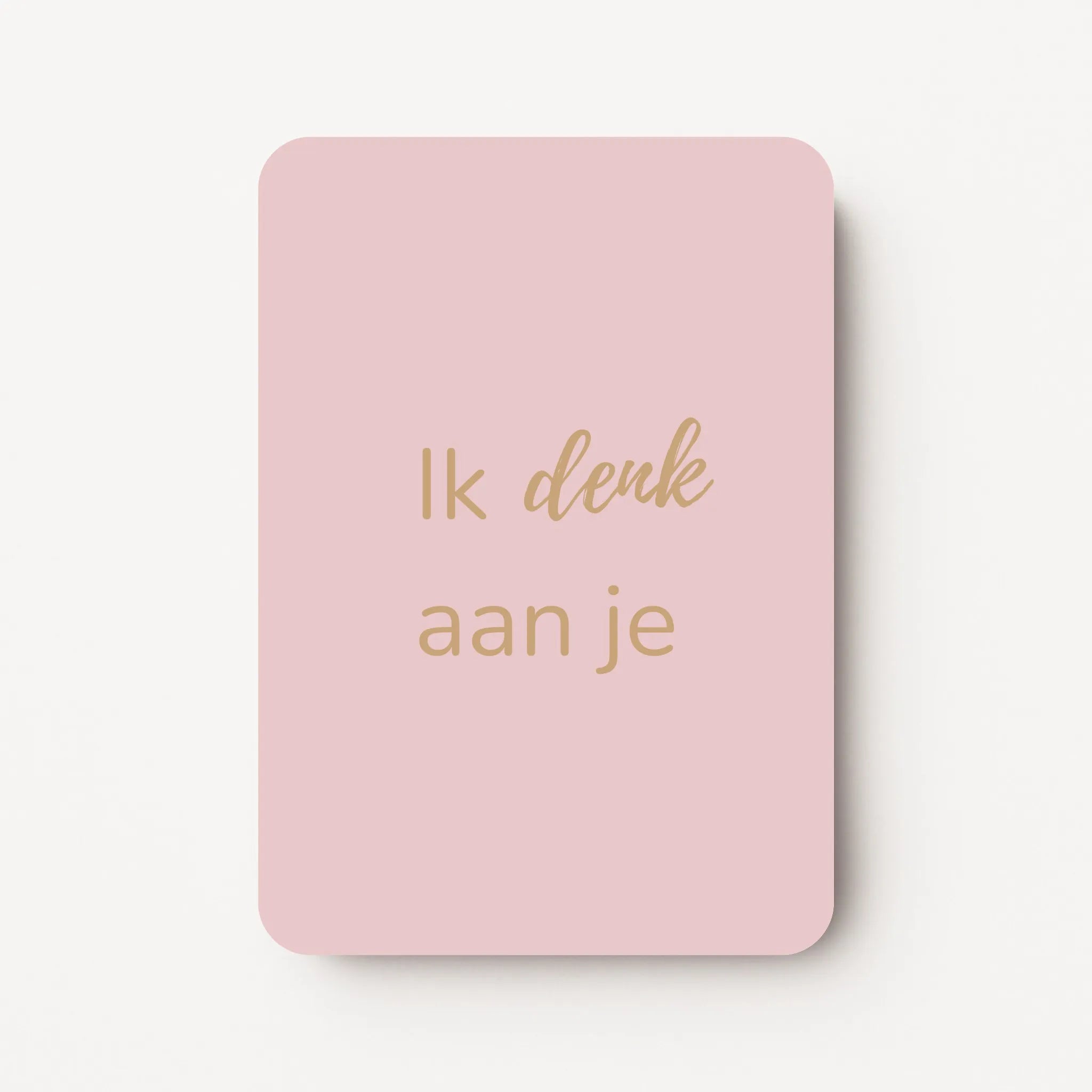 Staand minikaartje met goudbeige tekst ‘Ik denk aan je’, minimalistisch ontwerp op een zachte lichtroze achtergrond, flatlay op witte ondergrond.