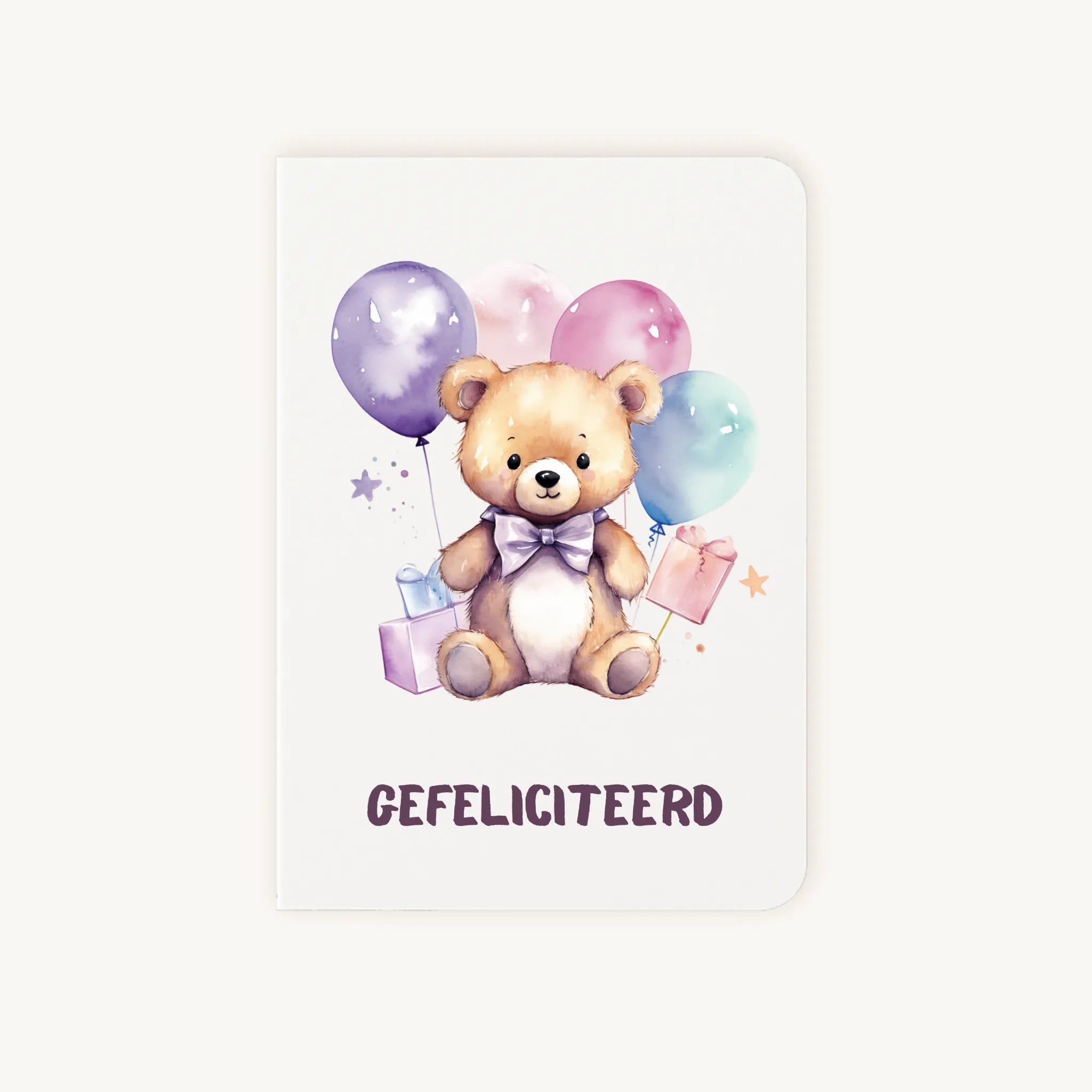 Staande dubbelgevouwen verjaardagskaart met lieve teddybeer met strik, ballonnen en cadeautjes, met tekst Gefeliciteerd, flatlay op lichte achtergrond.