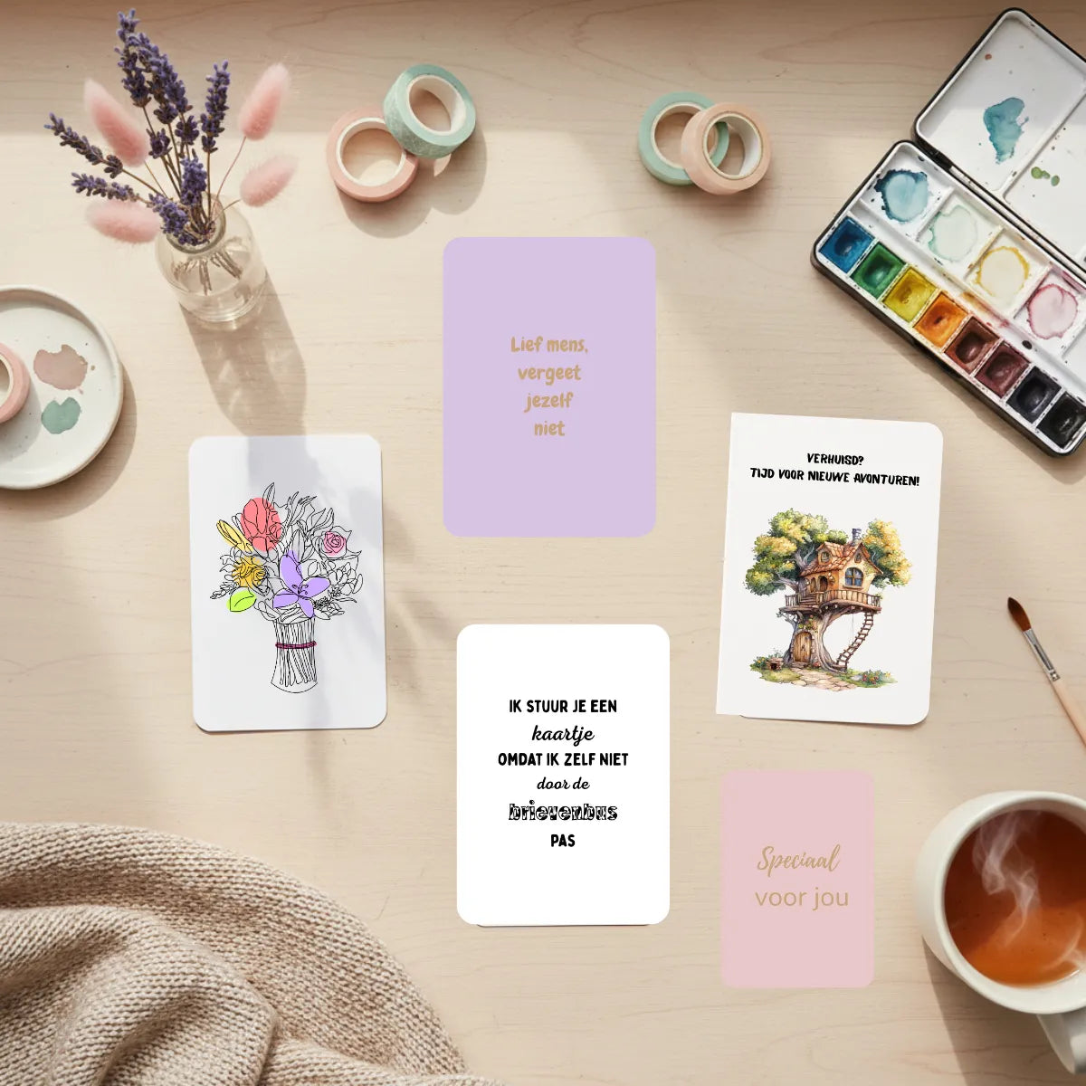 Wenskaarten collectie staand op houten bureau met afgeronde hoeken, omringd door droogbloemen en creatieve materialen