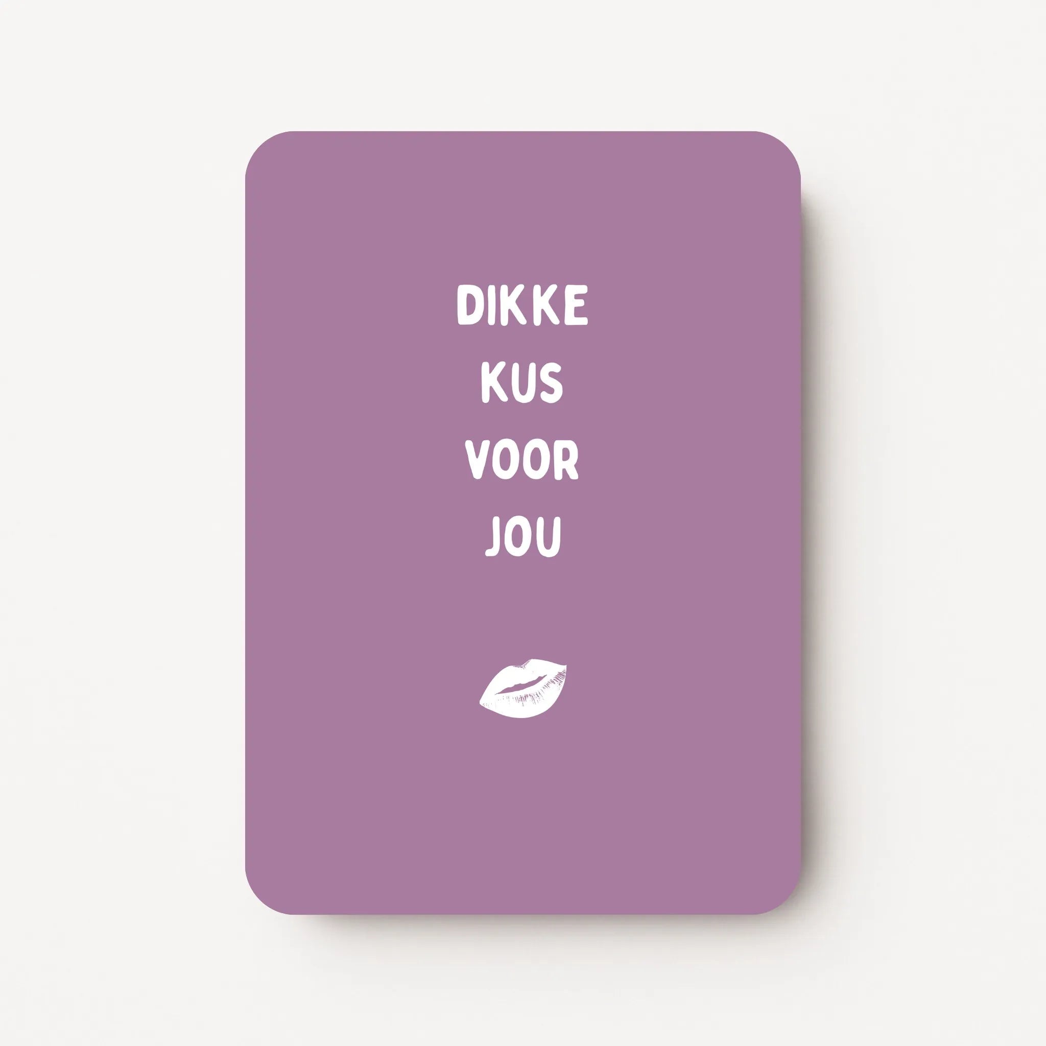 Staande kaart met tekst ‘Dikke kus voor jou’ in witte letters met witte lippenillustratie op een warme paarsroze achtergrond, flatlay op witte ondergrond.