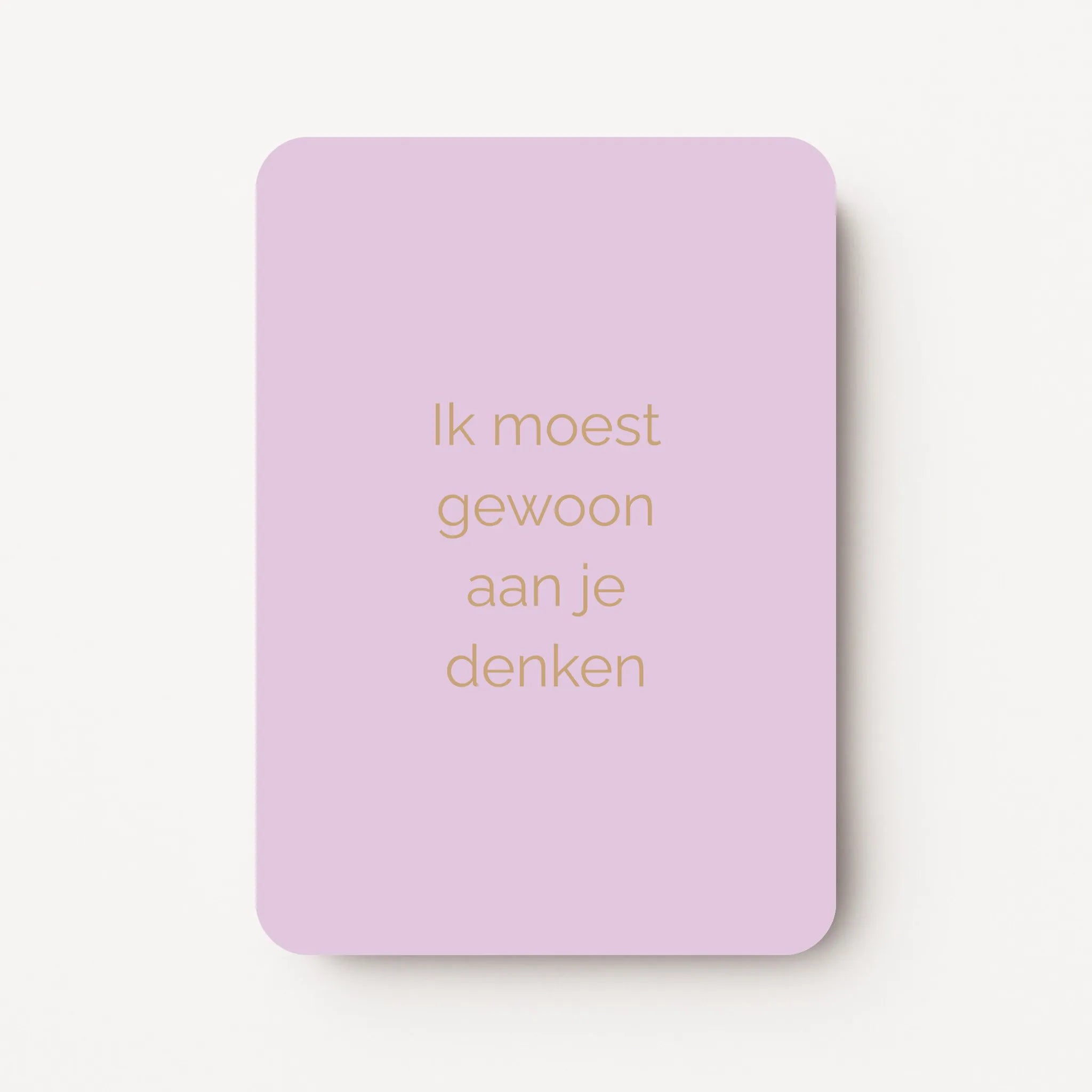 Staande kaart met tekst ‘Ik moest gewoon aan je denken’ in goudbruine letters op een zachte lila achtergrond, flatlay op witte ondergrond.