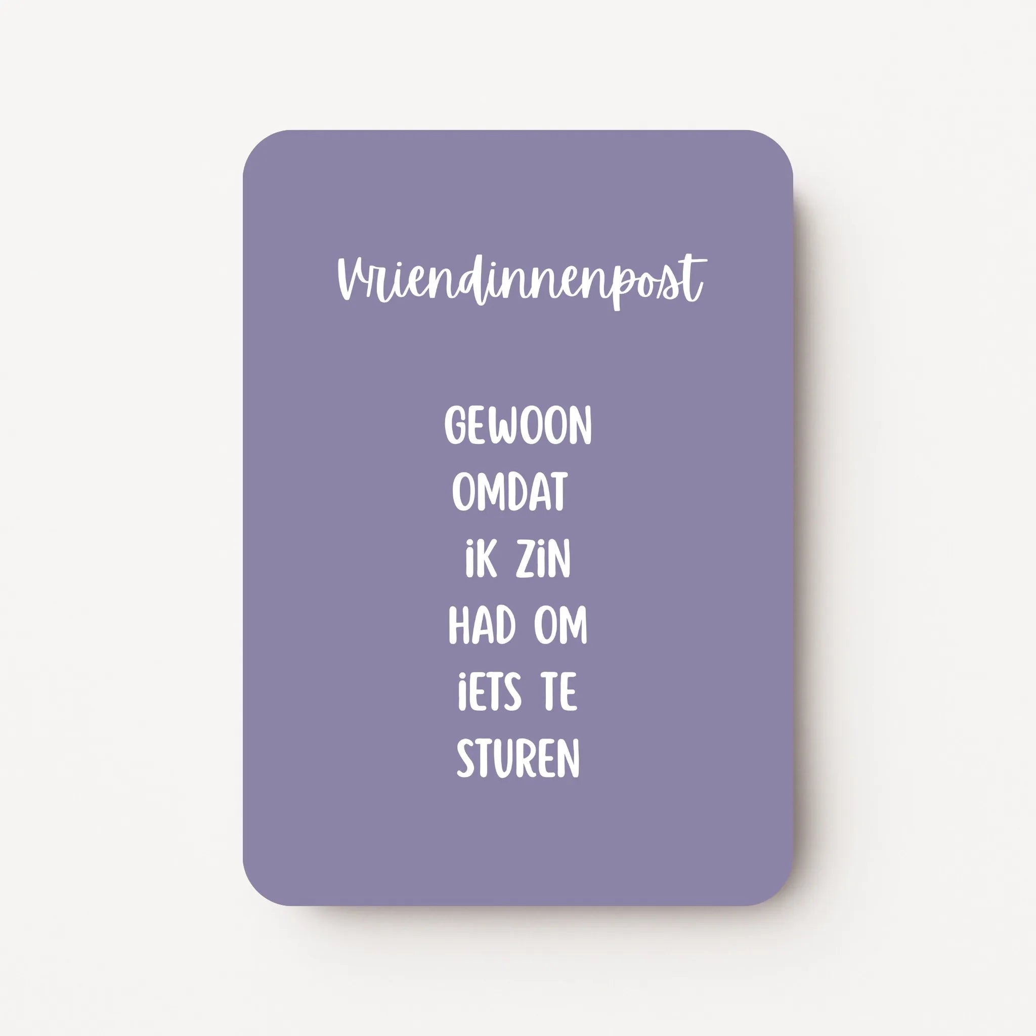 Staande kaart met tekst ‘Vriendinnenpost. Gewoon omdat ik zin had om iets te sturen’ in witte letters op een lavendelgrijze achtergrond, flatlay op witte ondergrond.