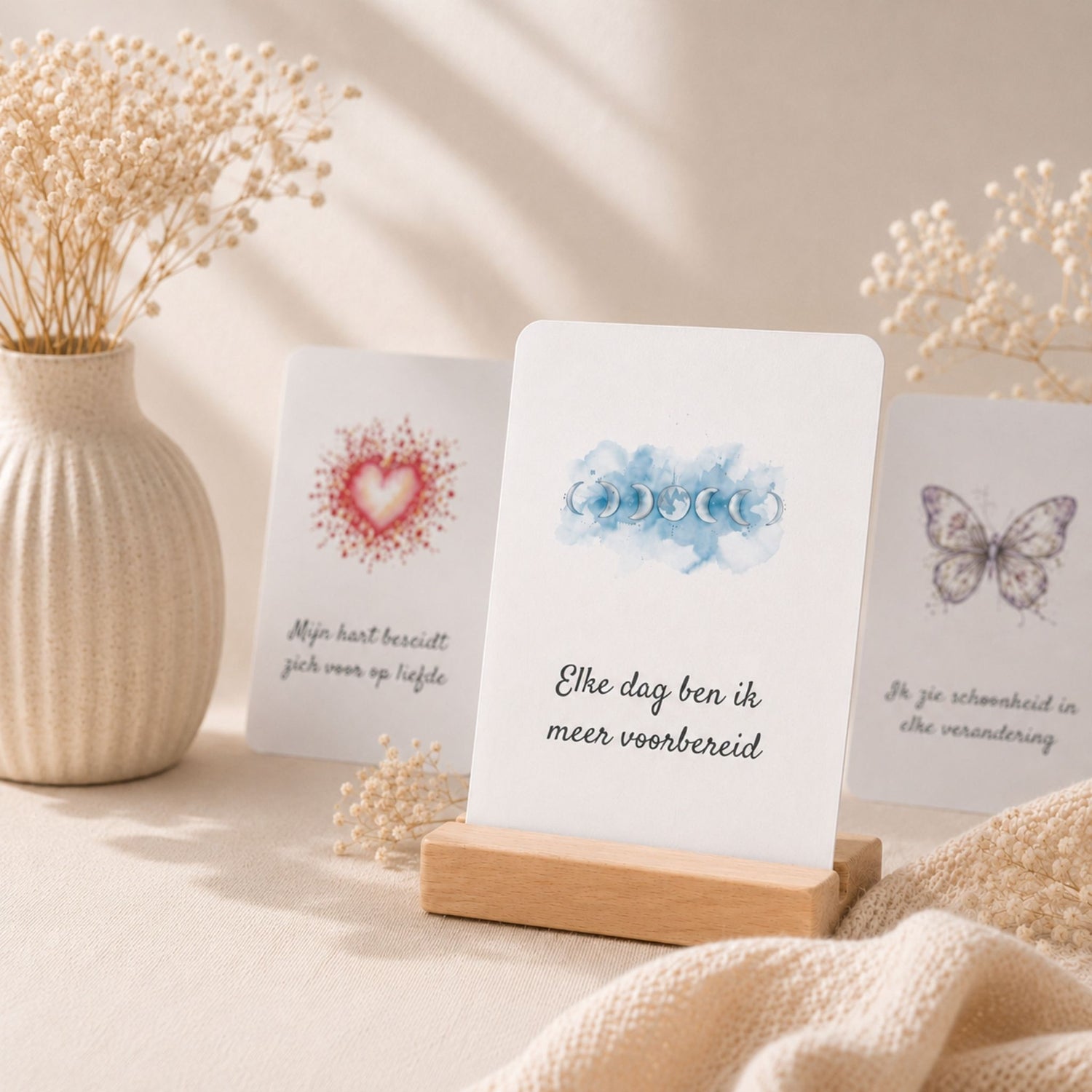 Drie Sam-fun affirmatiekaarten in een houten kaarthouder op een lichte linnen ondergrond, omringd door droogbloemen in warm natuurlijk daglicht. Een rustige, premium sfeerfoto die de collectie affirmatiekaarten laat zien.