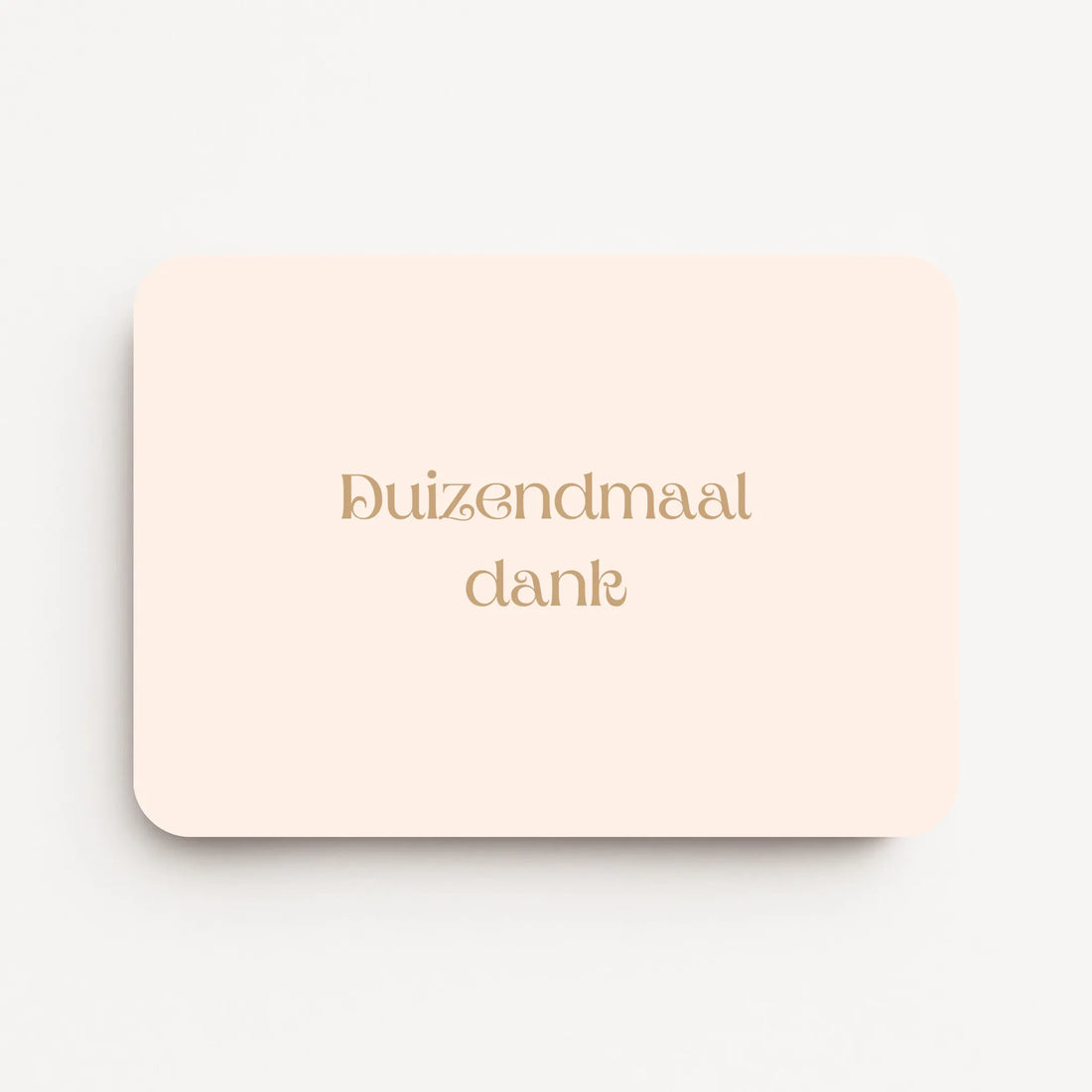 Liggende bedankkaart met tekst ‘Duizendmaal dank’ in sierlijke letters, goudbruine tekst op crème achtergrond, flatlay op witte ondergrond.