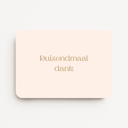 Liggende bedankkaart met tekst ‘Duizendmaal dank’ in sierlijke letters, goudbruine tekst op crème achtergrond, flatlay op witte ondergrond.