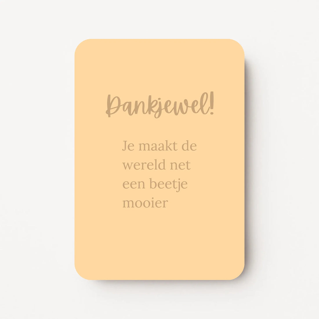 Staande bedankkaart met tekst ‘Dank je wel! je maakt de wereld net een beetje mooier’ in sierlijke letters, goudbruine tekst op goudgele/abrikoos achtergrond, flatlay op witte ondergrond.