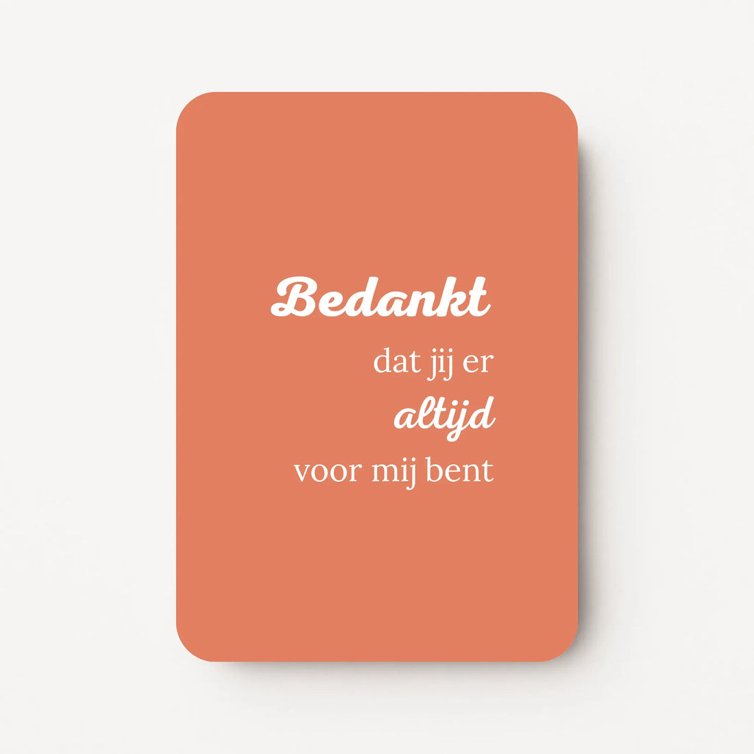 Staande bedankkaart met tekst ‘Bedankt dat jij er altijd voor mij bent’, witte letters op koraalroze achtergrond, flatlay op witte ondergrond.