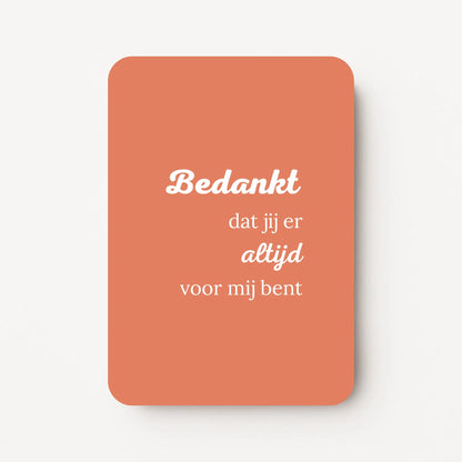 Staande bedankkaart met tekst ‘Bedankt dat jij er altijd voor mij bent’, witte letters op koraalroze achtergrond, flatlay op witte ondergrond.