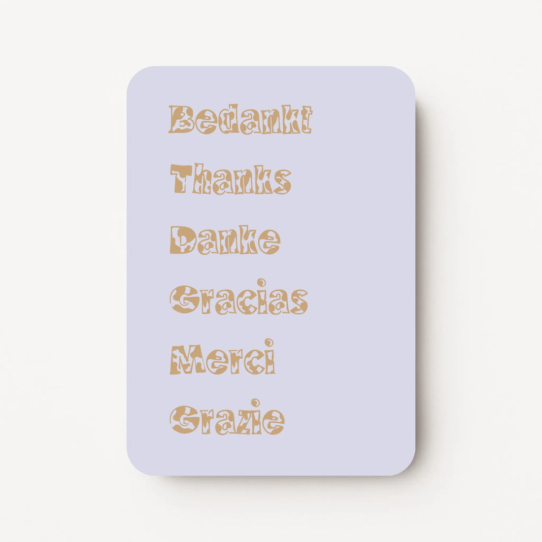 Staande bedankkaart met de woorden ‘Bedankt, Thanks, Danke, Gracias, Merci, Grazie’ onder elkaar in sierlijke letters, goudbruine tekst op lavendel achtergrond, flatlay op witte ondergrond.