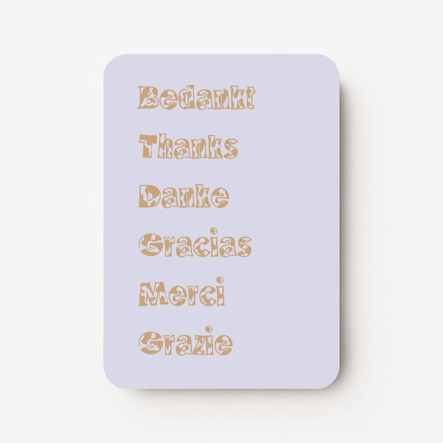 Staande bedankkaart met de woorden ‘Bedankt, Thanks, Danke, Gracias, Merci, Grazie’ onder elkaar in sierlijke letters, goudbruine tekst op lavendel achtergrond, flatlay op witte ondergrond.