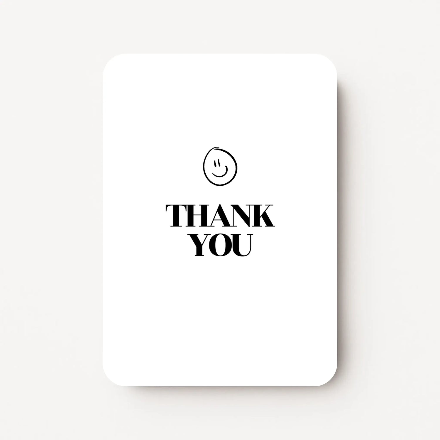Staande bedankkaart met tekst ‘THANK YOU’ in zwarte letters met een zwarte smiley erboven, flatlay op witte achtergrond.