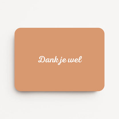 Liggende bedankkaart met tekst ‘Dank je wel’, witte letters op zandkleurige achtergrond, flatlay op witte ondergrond.
