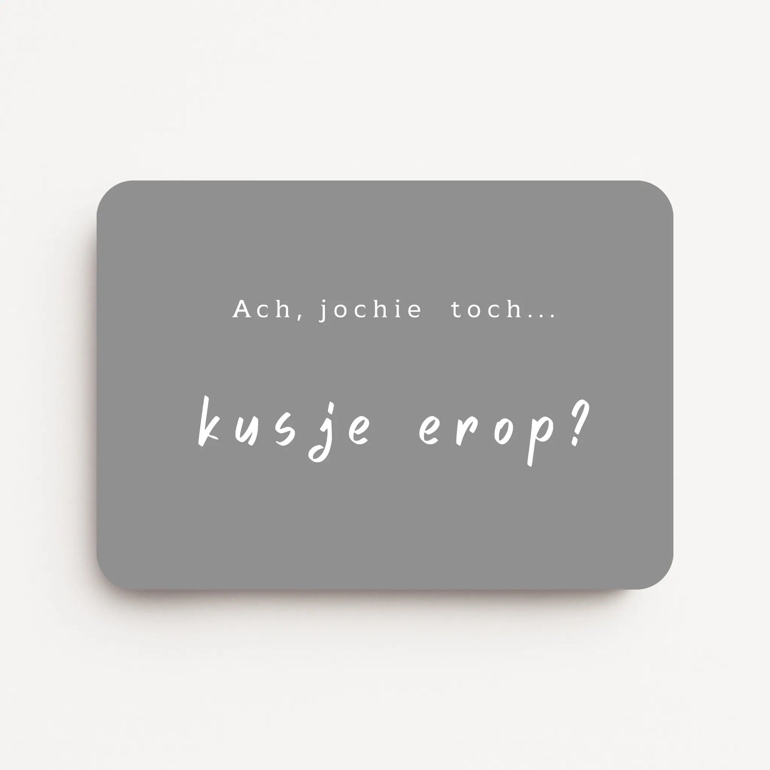 Liggende beterschapskaart met witte tekst ‘Ach, jochie toch... kusje erop?’ op een warme grijsbruine achtergrond, flatlay op witte ondergrond.