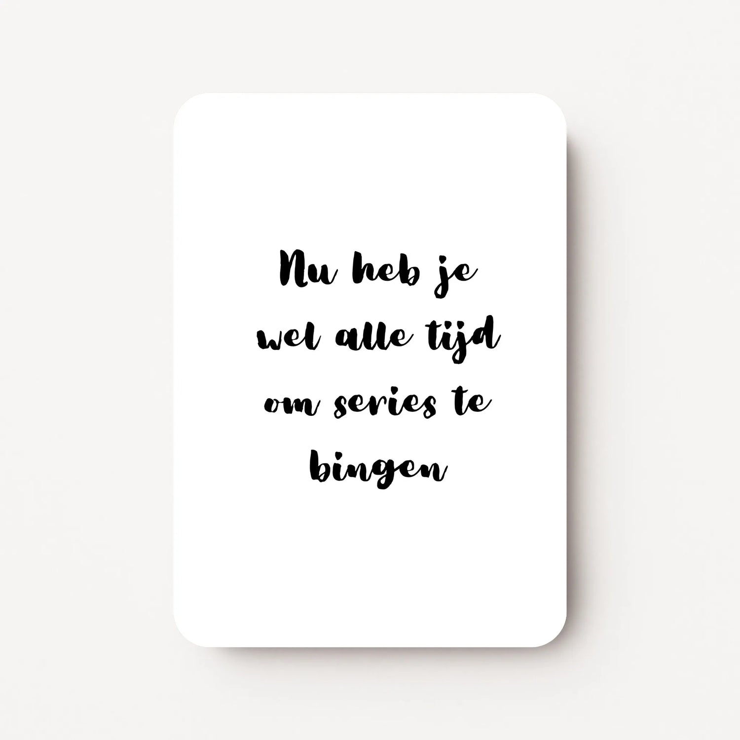 Staande beterschapskaart met zwarte tekst ‘Nu heb je wel alle tijd om series te bingen’ op witte achtergrond, minimalistisch ontwerp, flatlay op witte ondergrond.
