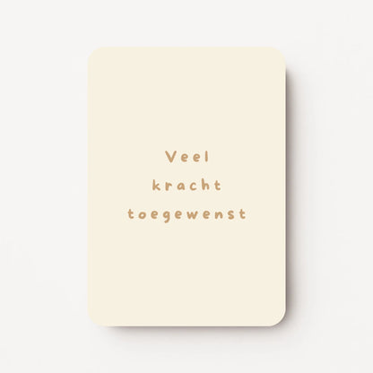 Staande beterschapskaart met zachte crème achtergrond en tekst in warme zandtint ‘Veel kracht toegewenst’, flatlay op witte ondergrond.