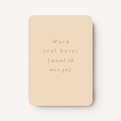 Staande beterschapskaart met licht perzikkleurige achtergrond en tekst in warme zandtint ‘Word snel beter (want ik mis je)’, flatlay op witte ondergrond.