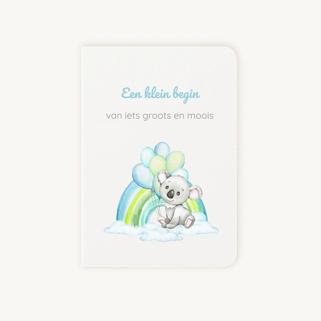 Staande dubbelgevouwen felicitatiekaart geboorte jongen met zachte pastelkleuren, koala met ballonnen en regenboog op wolkenachtergrond, met de tekst "Een klein begin van iets groots en moois", flatlay op lichte achtergrond.