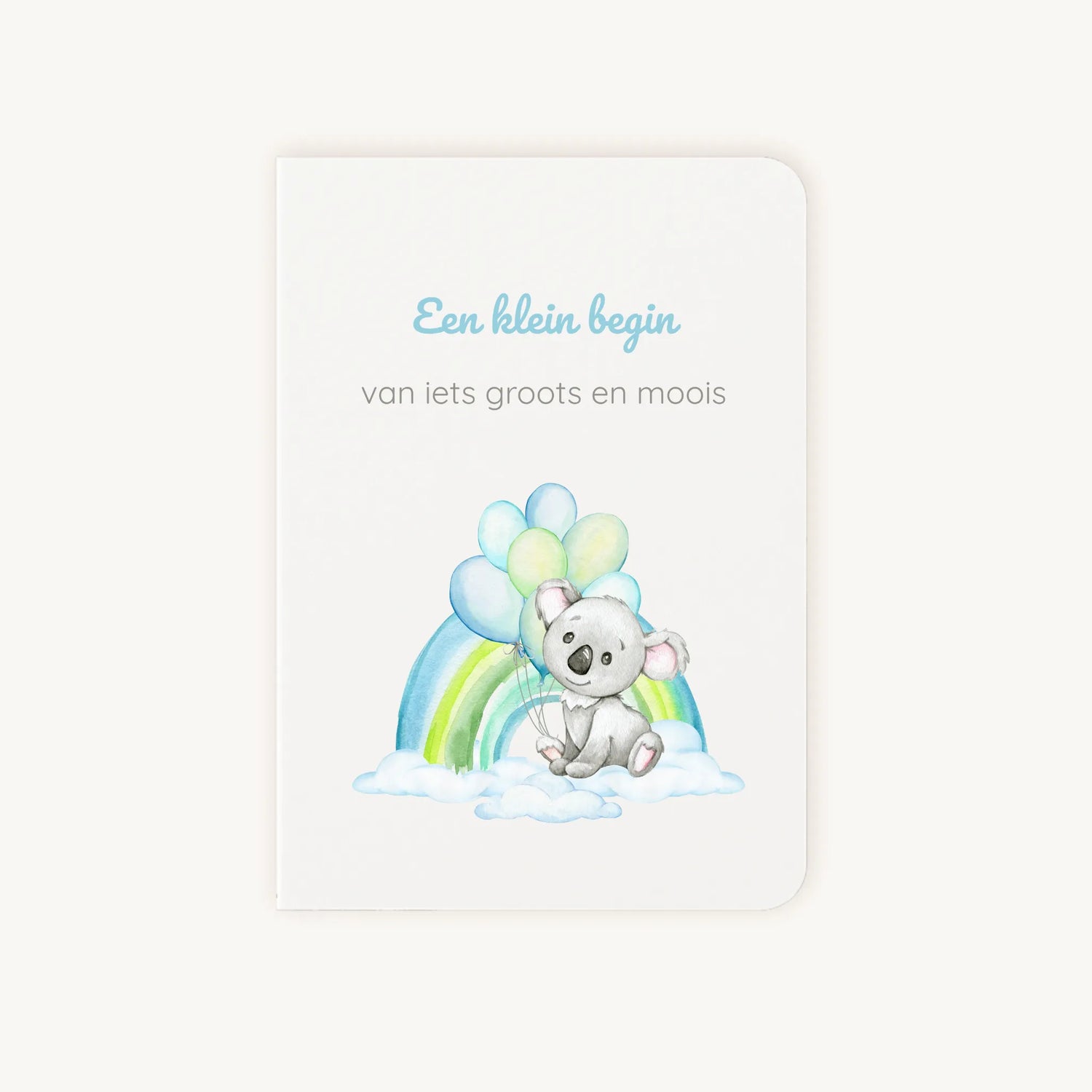 Staande dubbelgevouwen felicitatiekaart geboorte jongen met zachte pastelkleuren, koala met ballonnen en regenboog op wolkenachtergrond, met de tekst "Een klein begin van iets groots en moois", flatlay op lichte achtergrond.