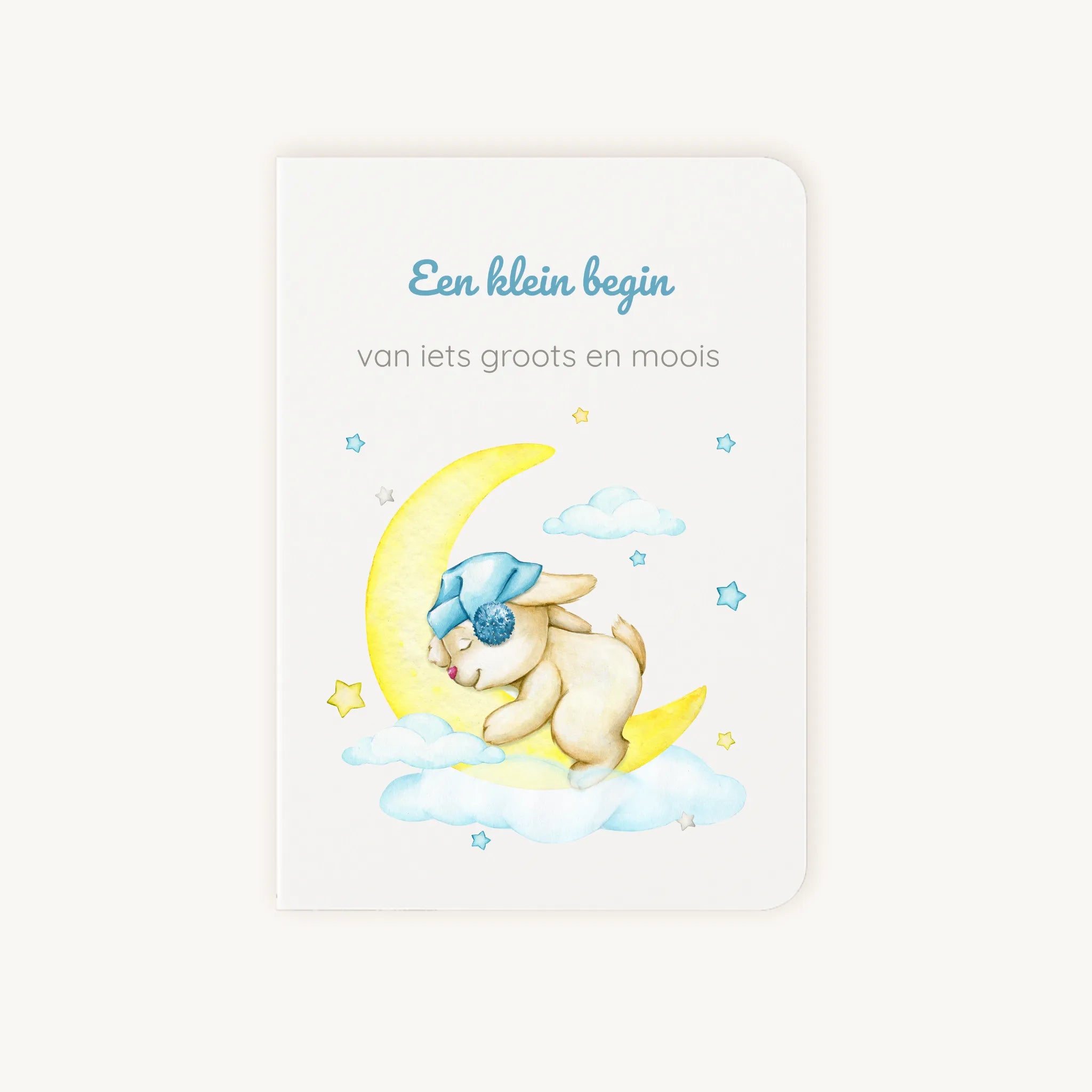 Staande dubbelgevouwen felicitatiekaart geboorte met zachte pastelkleuren, dromerig konijntje op gele maan met wolkjes en sterretjes, met de tekst "Een klein begin van iets groots en moois", flatlay op lichte achtergrond.