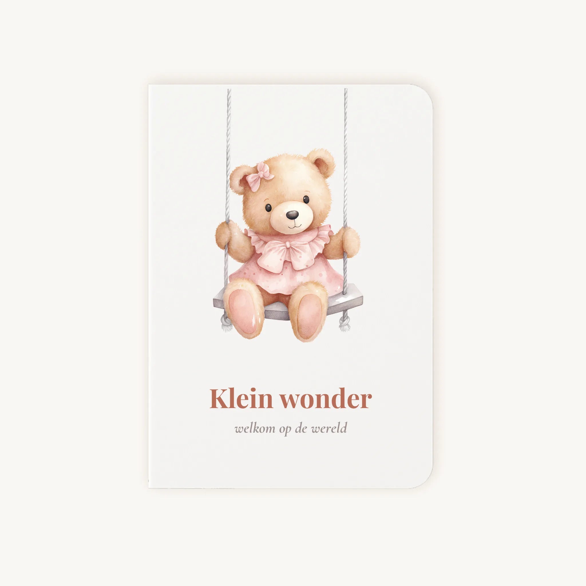 Staande dubbelgevouwen felicitatiekaart geboorte meisje met zachte pastelkleuren, teddybeer in roze jurkje op schommel, met de tekst "Klein wonder - welkom op de wereld", flatlay op lichte achtergrond.