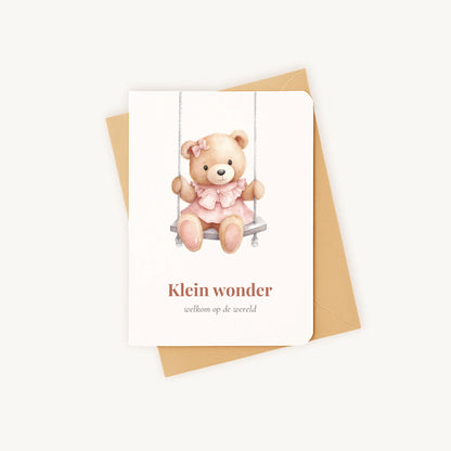 Staande kaart geboorte meisje met teddybeer op schommel op kraftenvelop.