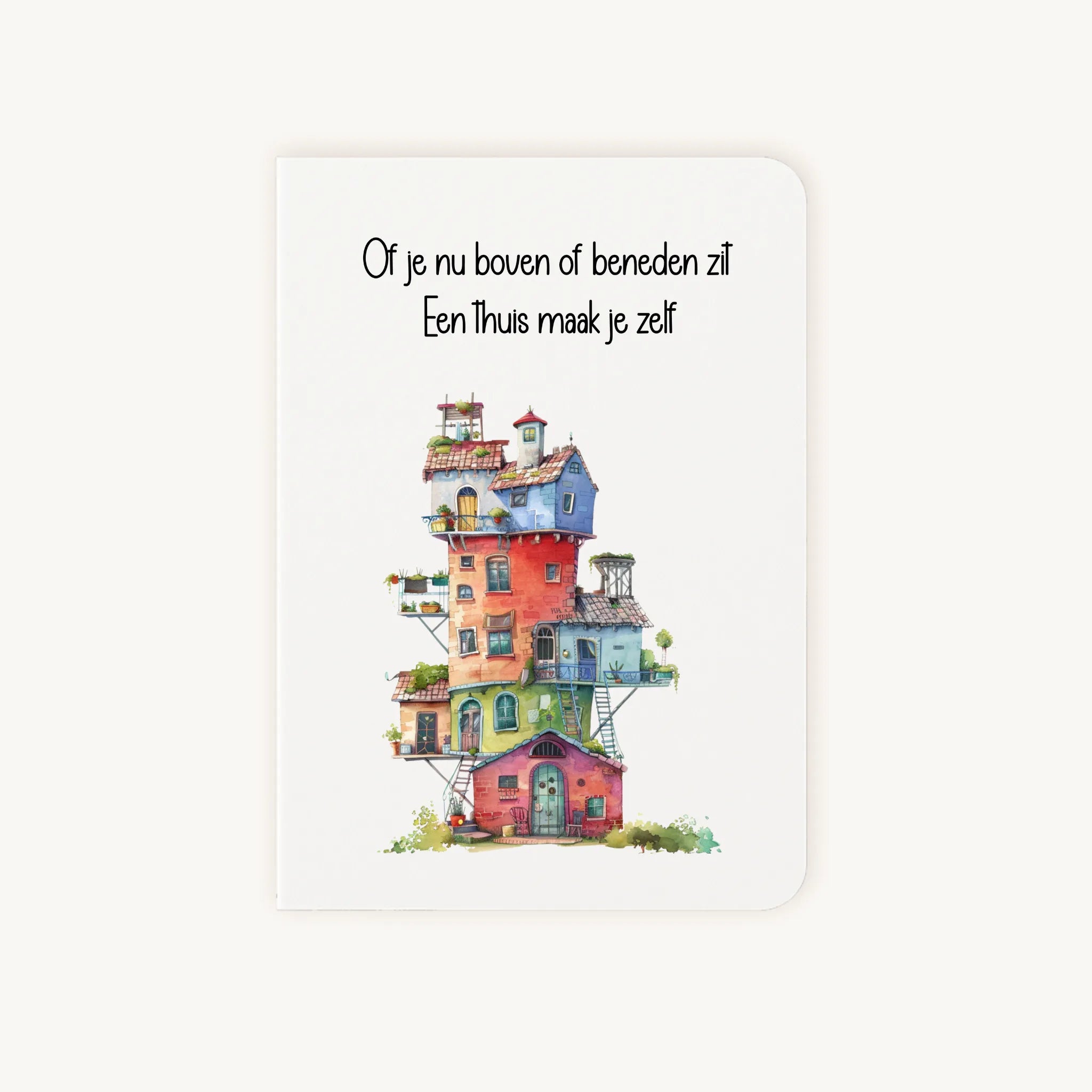 Staande dubbelgevouwen kaart nieuwe woning met afgeronde hoekjes en kleurrijke aquarelillustratie van een speels gestapeld huis, met de tekst Of je nu boven of beneden zit Een thuis maak je zelf, flatlay op lichte achtergrond.