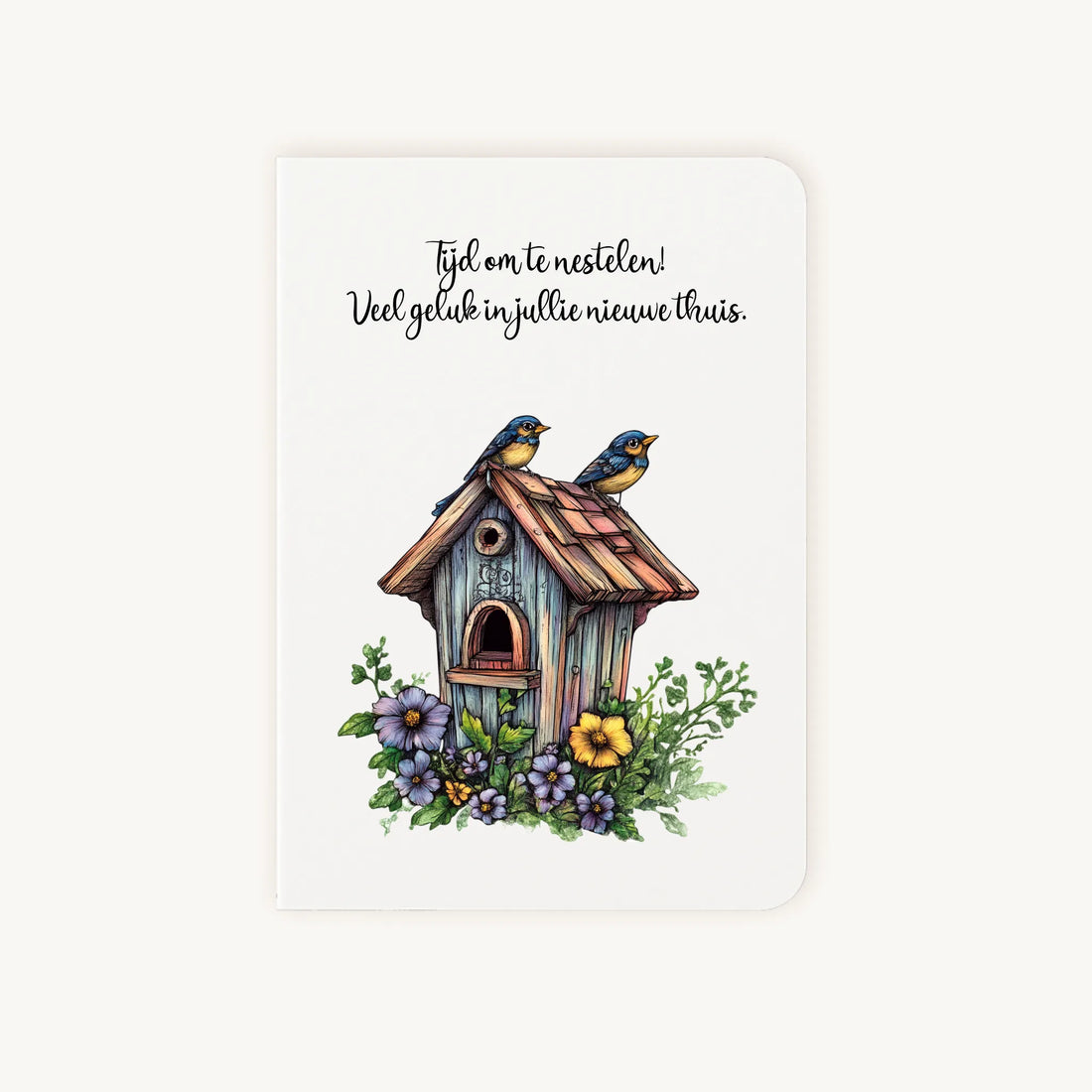 Staande dubbelgevouwen felicitatiekaart nieuwe woning met afgeronde hoekjes en sfeervolle aquarelillustratie van een houten vogelhuisje met bloemen en twee vogeltjes, met de tekst Tijd om te nestelen, flatlay op lichte achtergrond.