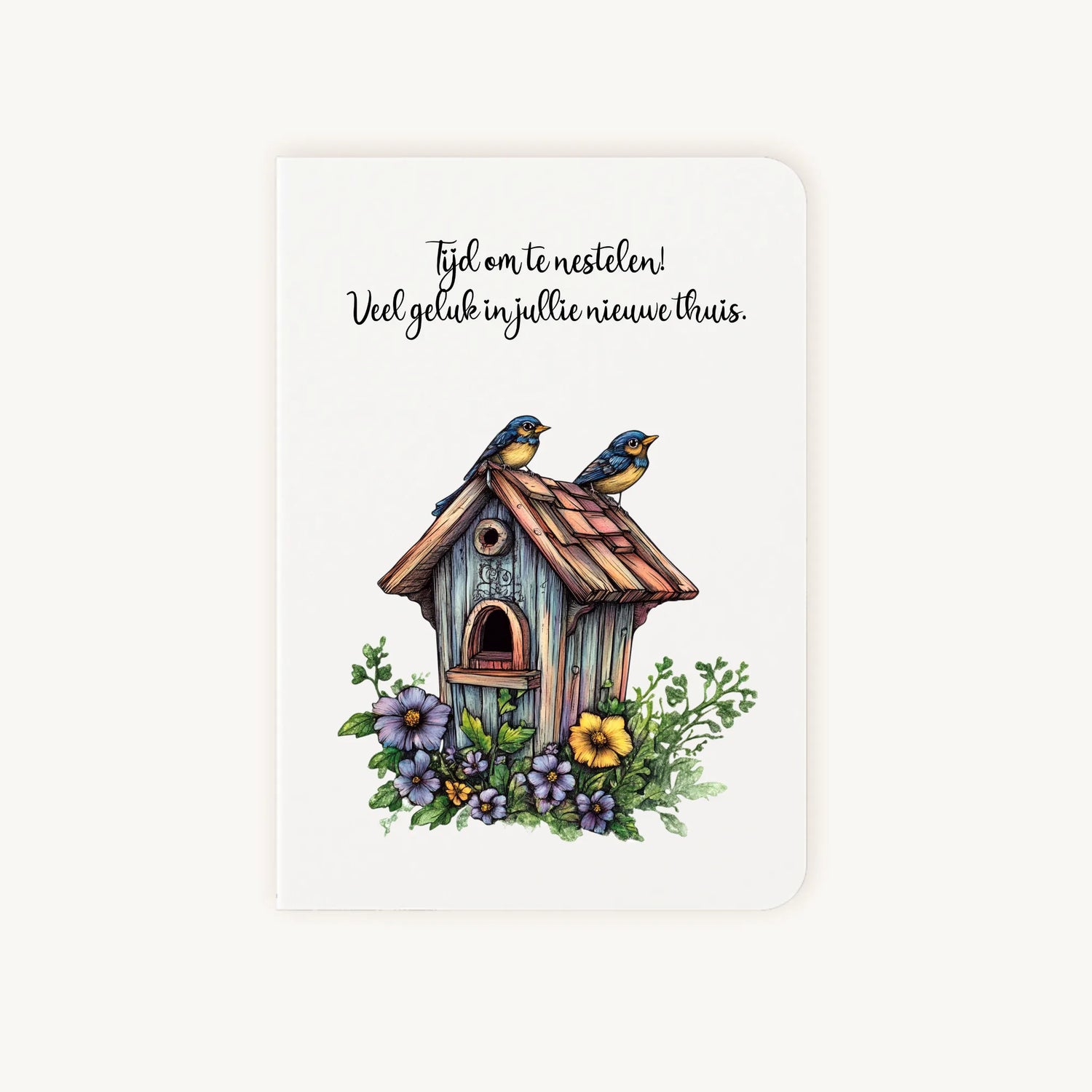 Staande dubbelgevouwen felicitatiekaart nieuwe woning met afgeronde hoekjes en sfeervolle aquarelillustratie van een houten vogelhuisje met bloemen en twee vogeltjes, met de tekst Tijd om te nestelen, flatlay op lichte achtergrond.