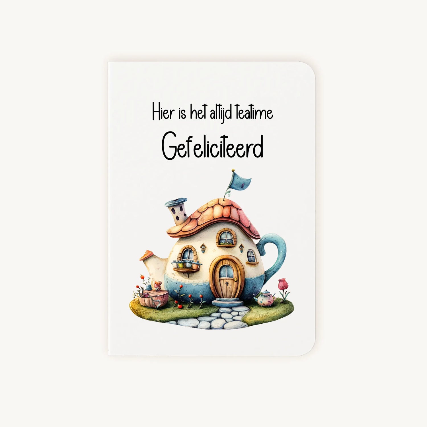 Staande dubbelgevouwen kaart nieuwe woning met afgeronde hoekjes en kleurrijke aquarelillustratie van een huisje in de vorm van een theepot, met de tekst Hier is het altijd teatime Gefeliciteerd, flatlay op lichte achtergrond.