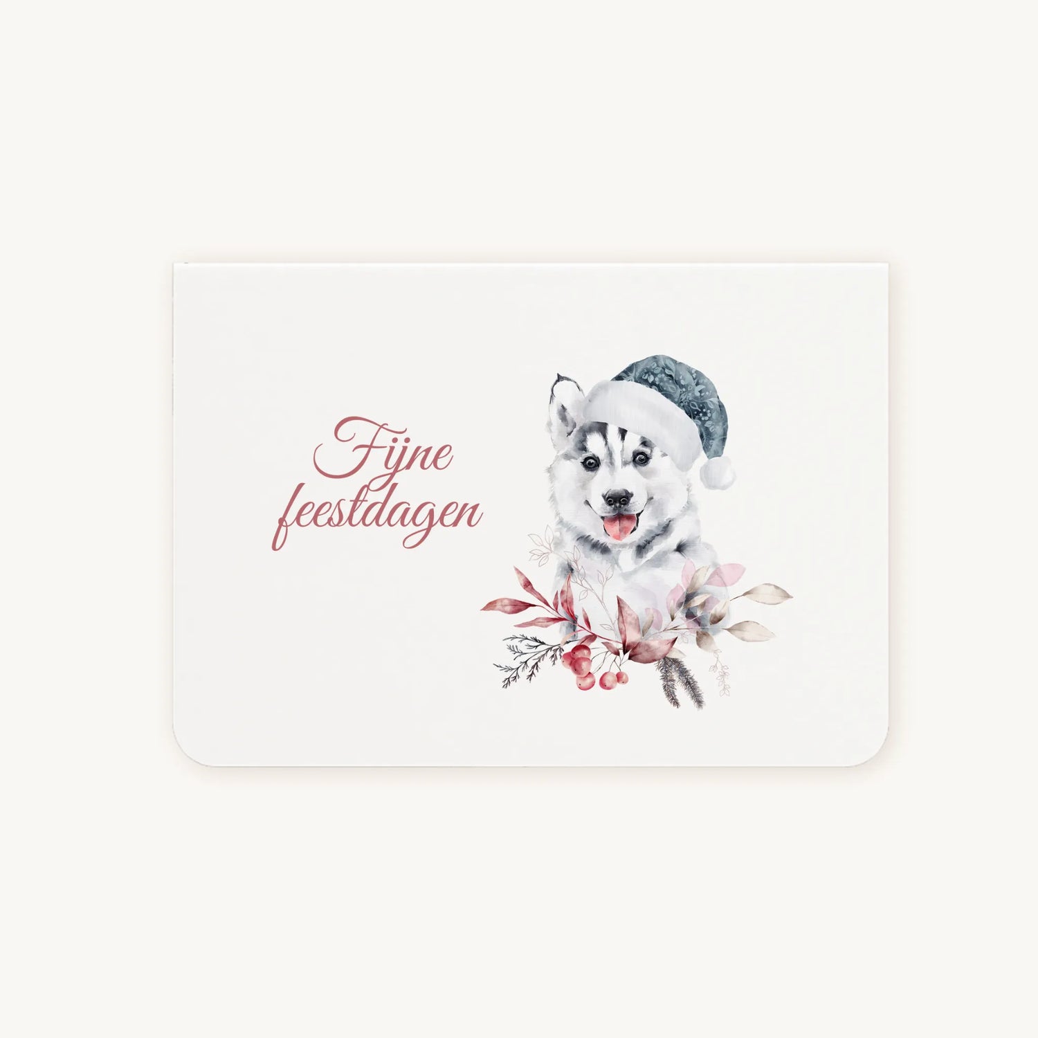 Liggende dubbelgevouwen kerstkaart met aquarelillustratie van een schattige husky-pup met blauwe kerstmanmuts, omringd door winterse bladeren en bessen, sierlijke tekst ‘fijne feestdagen’, flatlay op lichte achtergrond.