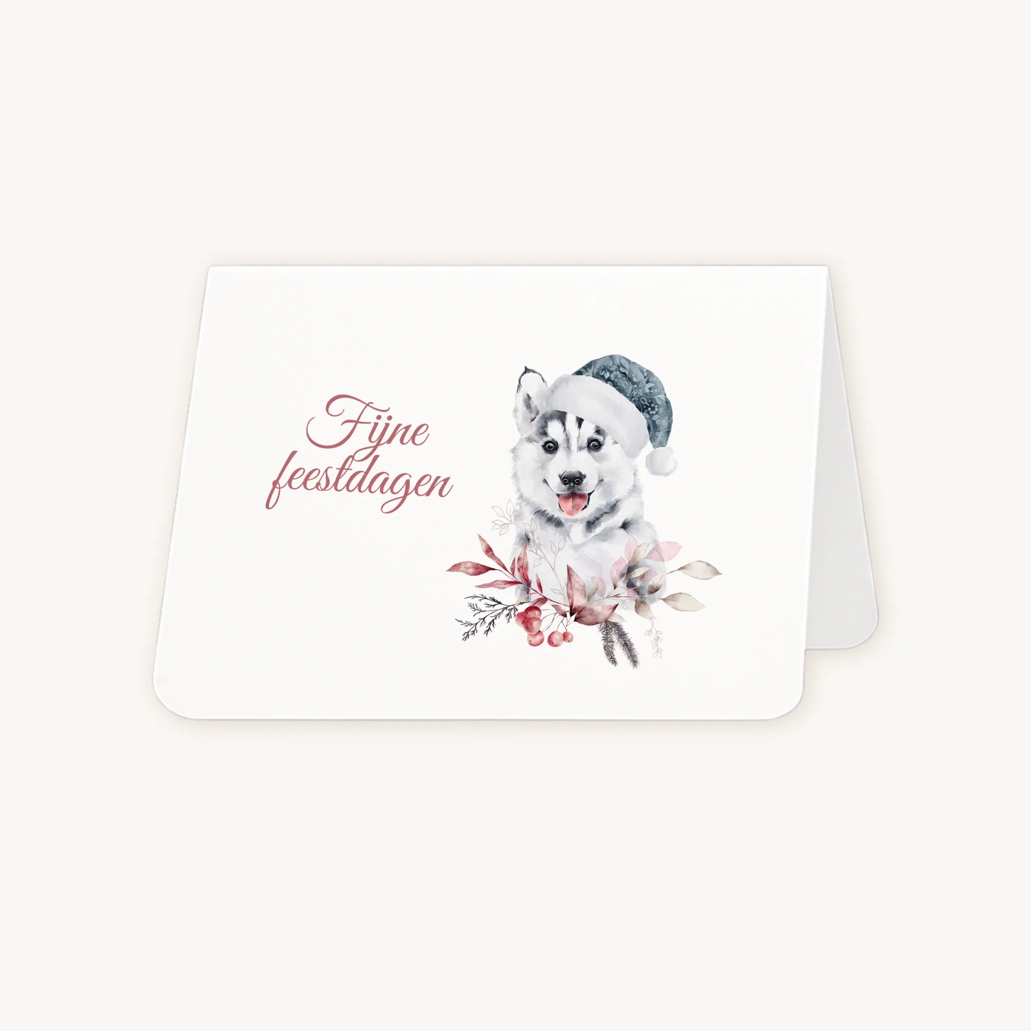 Half geopende liggende kerstkaart met aquarel husky-pup met blauwe kerstmanmuts en winterse bladeren en bessen, sierlijke tekst ‘fijne feestdagen’, op lichte achtergrond.