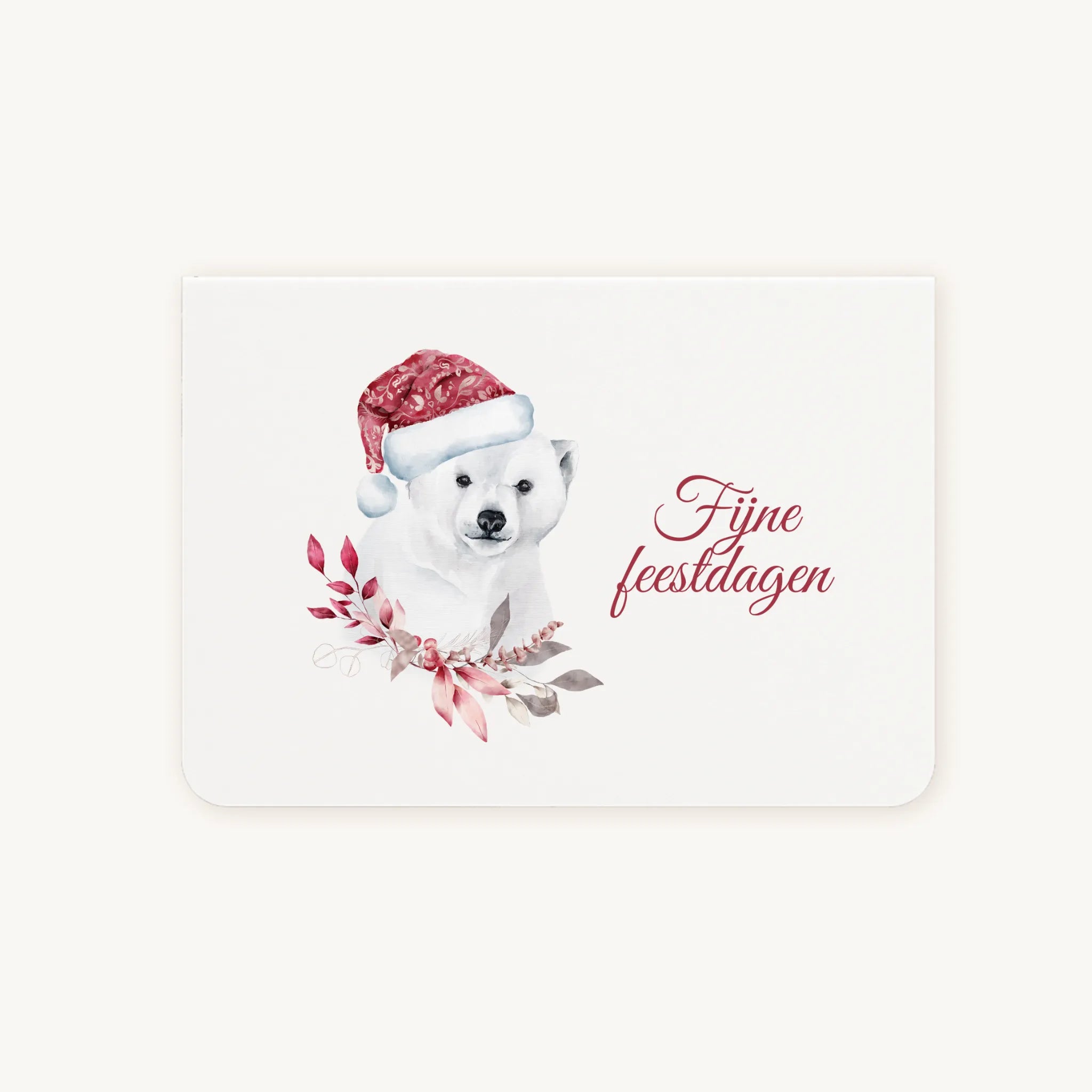 Liggende dubbelgevouwen kerstkaart met aquarelillustratie van een schattige ijsbeer met rode kerstmuts, omringd door winterse bladeren, sierlijke tekst ‘fijne feestdagen’, flatlay op lichte achtergrond.