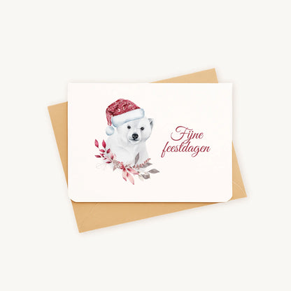 Liggende kerstkaart met aquarel ijsbeer met rode kerstmuts en winterse bladeren, sierlijke tekst ‘fijne feestdagen’, op kraftenvelop op lichte achtergrond.