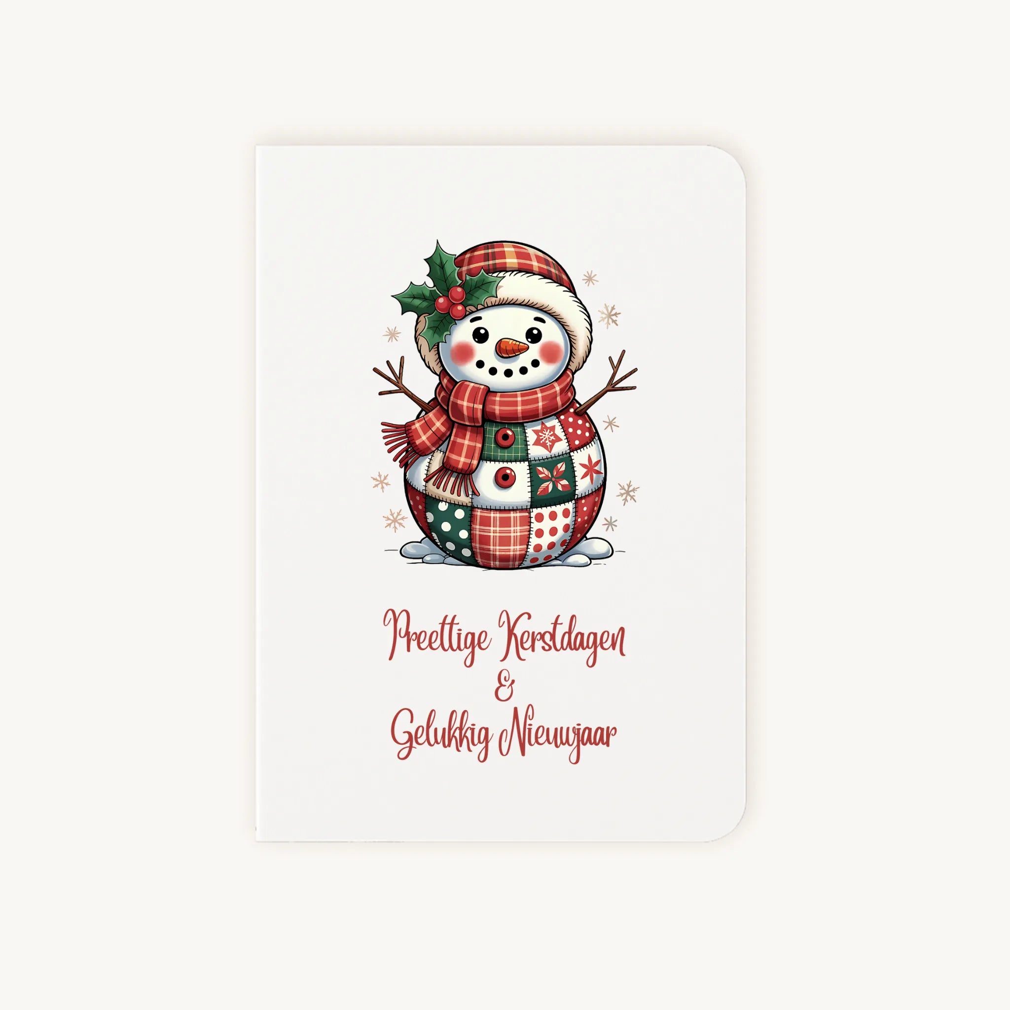 Staande dubbelgevouwen kerstkaart met kleurrijke patchwork sneeuwpop in aquarelstijl en sierlijke tekst ‘Prettige Kerstdagen &amp; Gelukkig Nieuwjaar’, flatlay op lichte achtergrond.