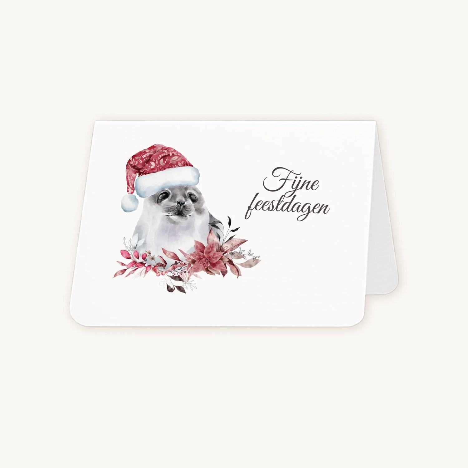 Half geopende liggende kerstkaart met aquarel zeehond met kerstmanmuts en winterse bloemen en blaadjes, sierlijke tekst ‘fijne feestdagen’, op lichte achtergrond.
