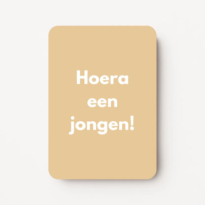 Staande minikaart met witte tekst "Hoera een jongen!", minimalistisch ontwerp op een zachte honingbeige achtergrond.