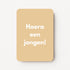 Staande minikaart met witte tekst "Hoera een jongen!", minimalistisch ontwerp op een zachte honingbeige achtergrond.
