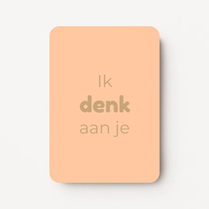 Staande minikaart met goudbeige tekst "Ik denk aan je", minimalistisch ontwerp op een warme perzikroze achtergrond.