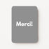 Staande minikaart met witte tekst "Merci!", minimalistisch ontwerp op een middengrijze achtergrond.