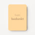 Staande minikaart met goudbeige tekst "Super bedankt", minimalistisch ontwerp op een zachte abrikoosgele achtergrond.