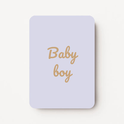 Staand minikaartje met tekst ‘Baby boy’ in goudbeige letters, minimalistisch ontwerp op zachte lavendelgrijze achtergrond, flatlay op witte ondergrond.