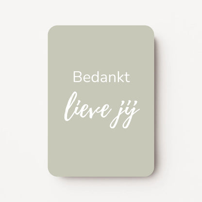 Staand minikaartje met witte tekst ‘Bedankt lieve jij’ op licht taupe-grijze achtergrond, minimalistisch ontwerp, flatlay op witte ondergrond.