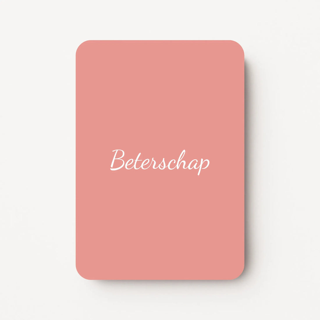 Staand minikaartje met tekst ‘Beterschap’ in witte letters, minimalistisch ontwerp op zachte oudroze achtergrond, flatlay op witte ondergrond.