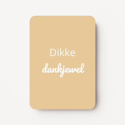 Staand minikaartje met witte tekst ‘Dikke dankjewel’ op zachte geel-beige achtergrond, minimalistisch ontwerp, flatlay op witte ondergrond.