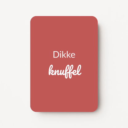 Staand minikaartje met witte tekst ‘Dikke knuffel’, minimalistisch ontwerp op een diepe bordeauxrode achtergrond, flatlay op witte ondergrond.