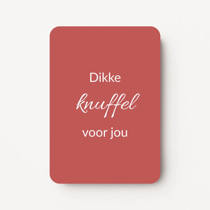 Staand minikaartje met tekst ‘Dikke knuffel voor jou’ in witte letters, minimalistisch ontwerp op warme bordeauxrode achtergrond, flatlay op witte ondergrond.