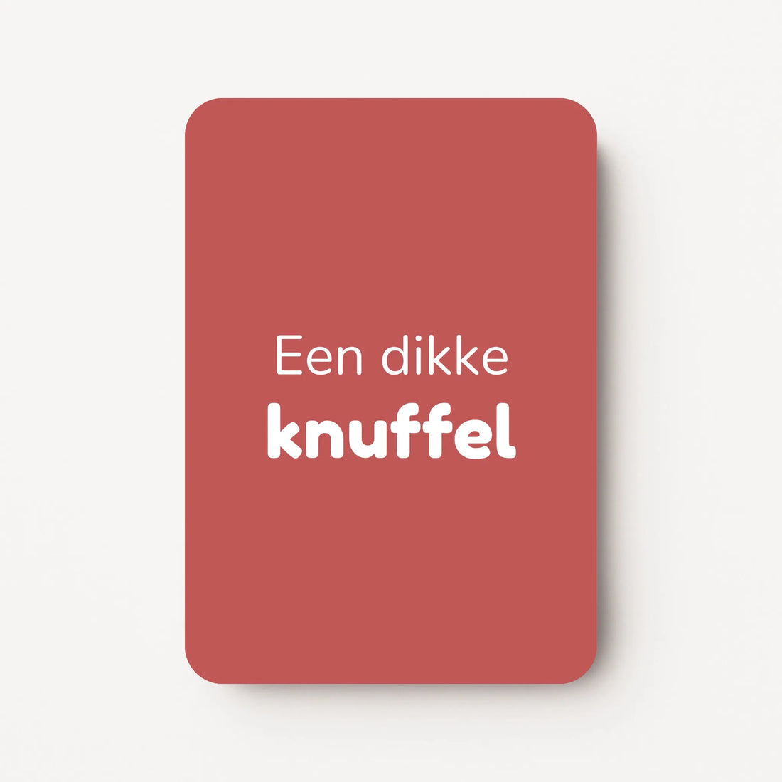 Staand minikaartje met witte tekst ‘Een dikke knuffel’, minimalistisch ontwerp op een warme dieproze achtergrond, flatlay op witte ondergrond.