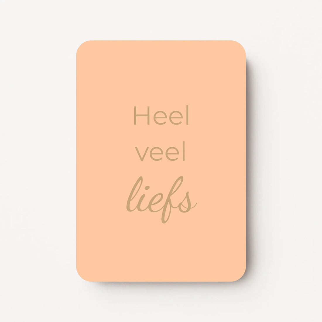Staand minikaartje met goudbeige tekst ‘Heel veel liefs’, minimalistisch ontwerp op een zachte abrikooskleurige achtergrond, flatlay op witte ondergrond.
