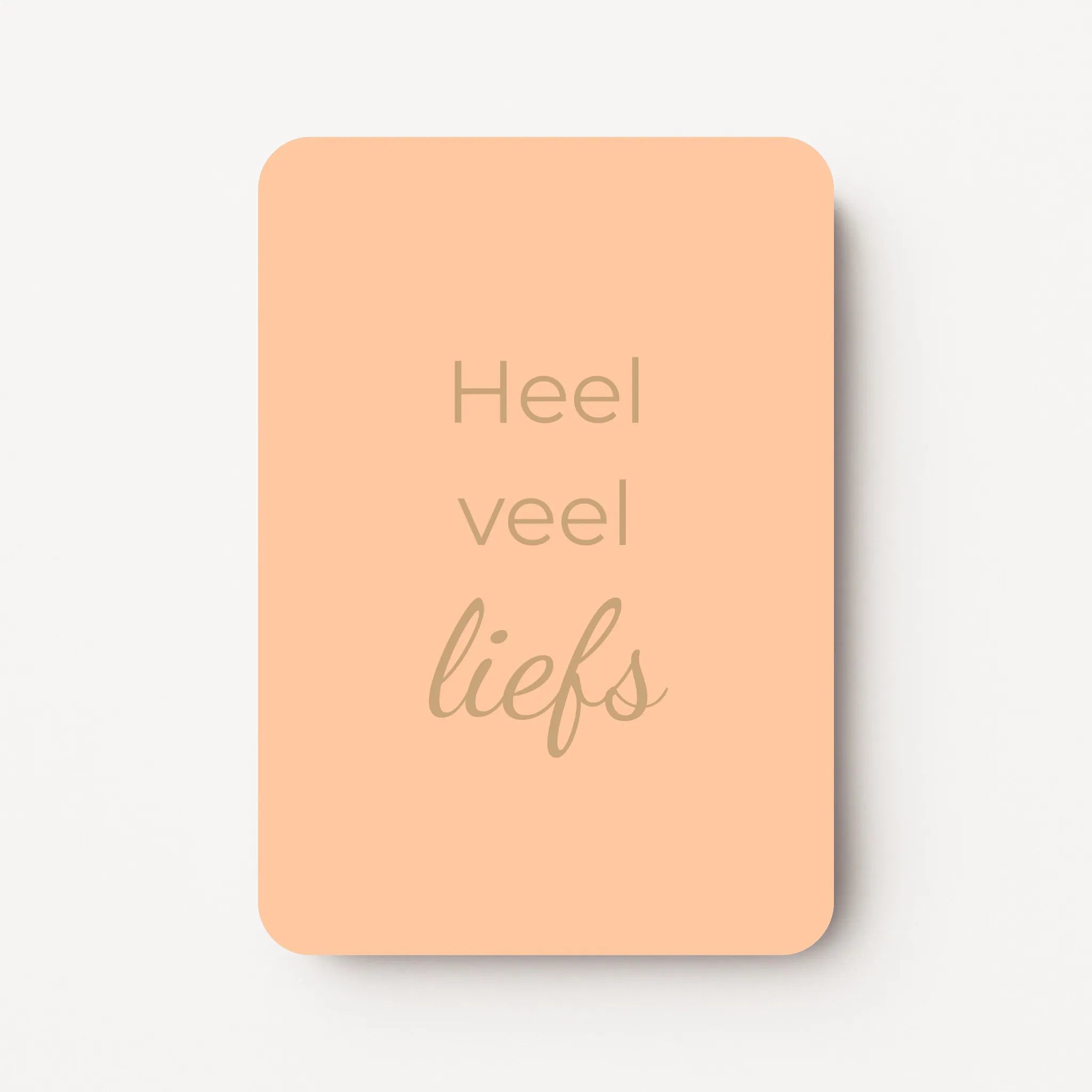 Staand minikaartje met goudbeige tekst ‘Heel veel liefs’, minimalistisch ontwerp op een zachte abrikooskleurige achtergrond, flatlay op witte ondergrond.